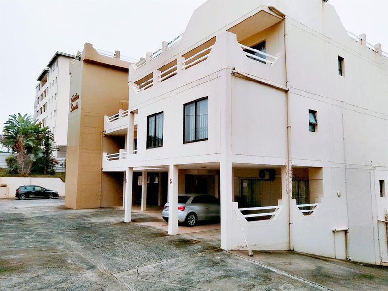 Exterior view of the apartment building featuring covered ground-level parking bays and upper-level balconies with a concrete driveway approach.