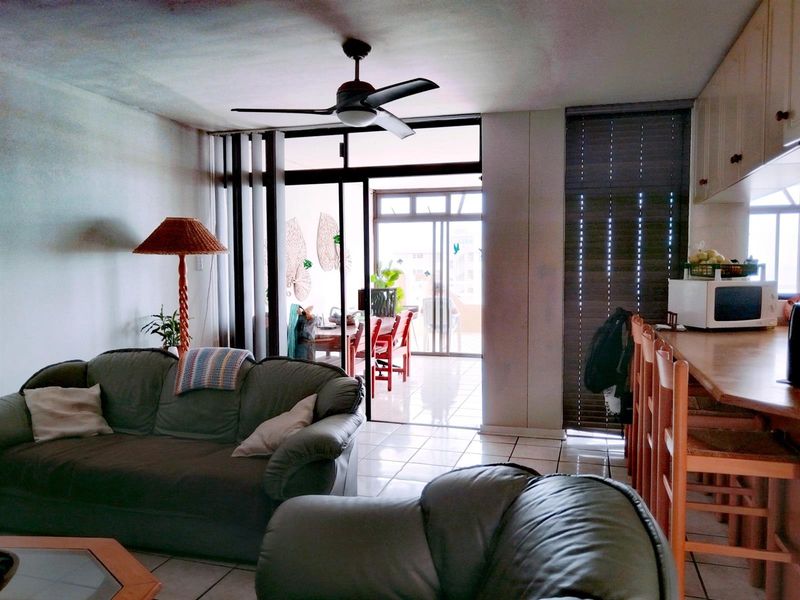 Open plan living area featuring tiled floors, a ceiling fan, and a breakfast bar, with direct access to an outdoor balcony through sliding glass doors.