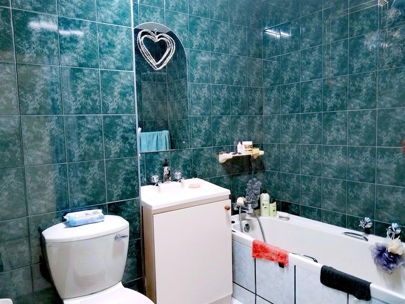 A bathroom featuring dark green marble-effect wall tiles, a white vanity unit with basin, and a standard bathtub.