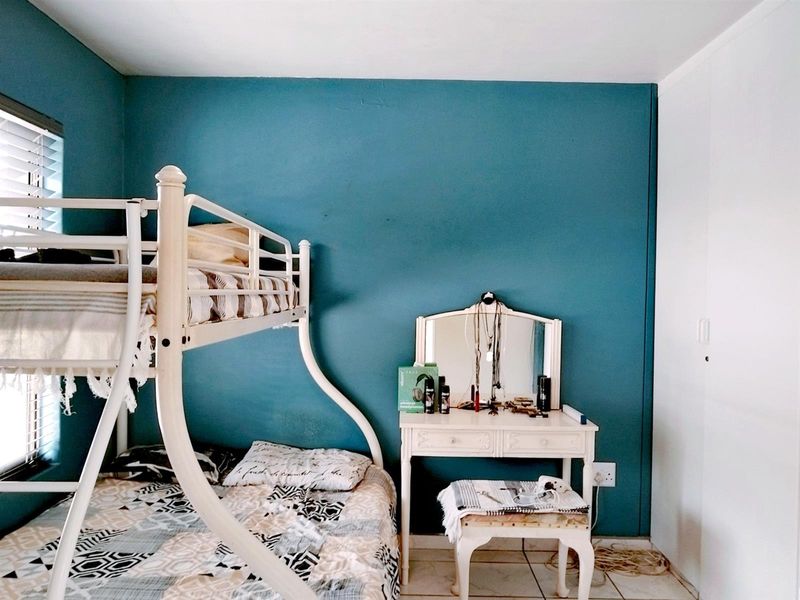 A bedroom featuring tiled flooring, a built-in cupboard, and venetian blinds, finished with a bold blue accent wall.