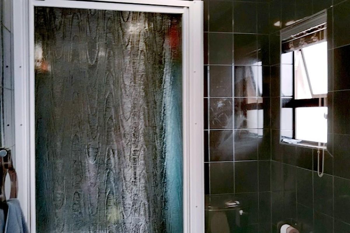 A compact bathroom featuring dark wall tiles, a shower enclosure, and a toilet, with visible signs of wear on the ceiling.