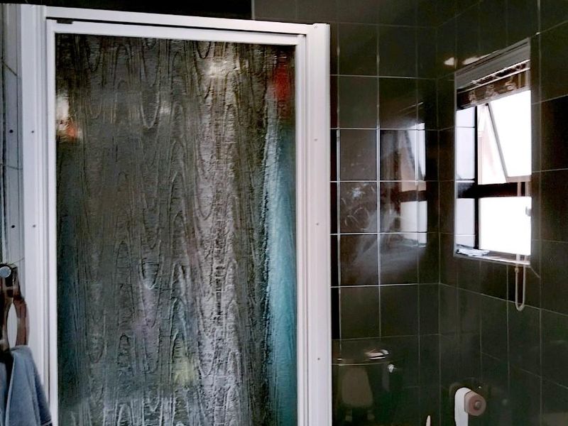A compact bathroom featuring dark wall tiles, a shower enclosure, and a toilet, with visible signs of wear on the ceiling.