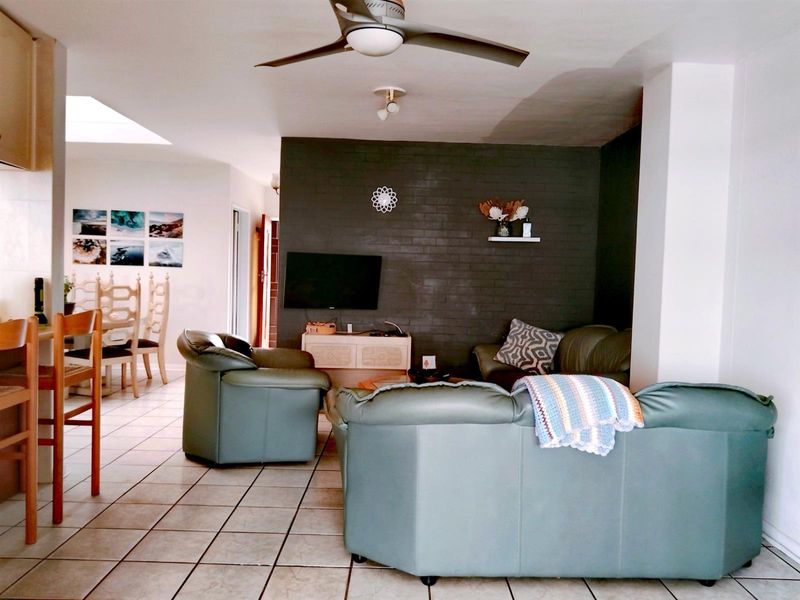 Open-plan living area featuring ceramic floor tiles, a ceiling fan, a skylight, and a dark-painted exposed brick feature wall.