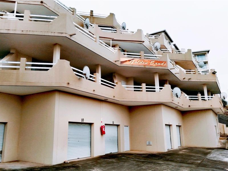 Exterior view of the Golden Sands apartment complex featuring multiple levels of balconies and ground-floor roller shutter garage doors.