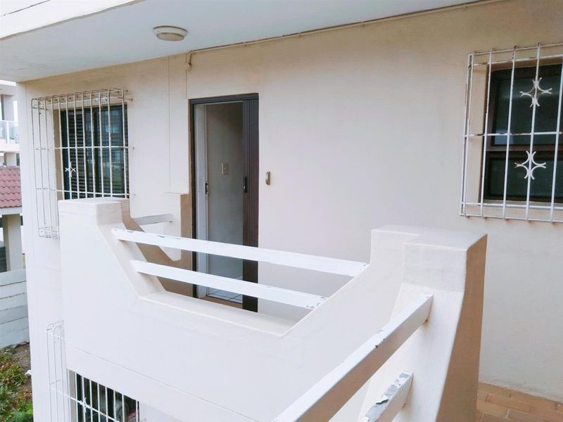 A functional balcony area featuring security bars on windows and a simple railing, providing access to the apartment interior.