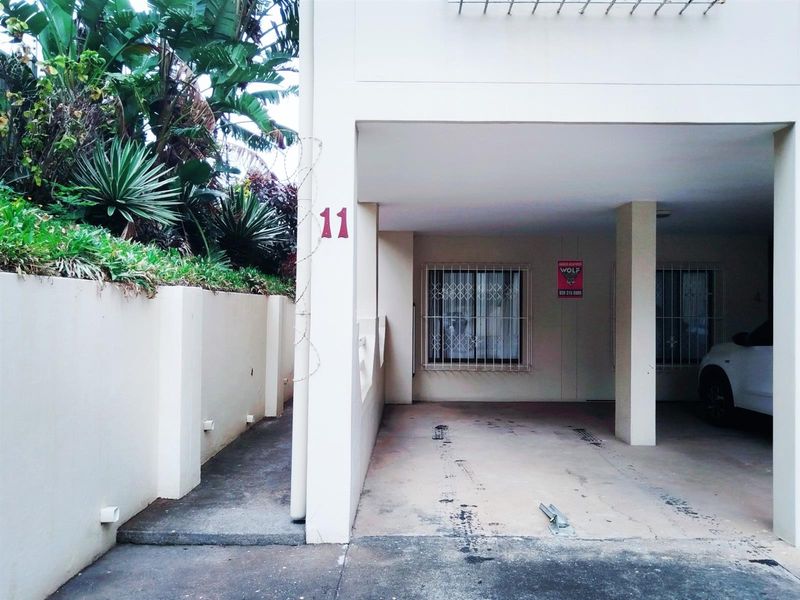 Covered parking area for apartment unit 11, featuring concrete flooring, security bars on windows, and an adjacent retaining wall with landscaped garden.