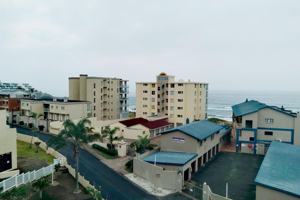 Aerial view of the apartment complex grounds, showing surrounding buildings, paved driveways, parking areas, and proximity to the coastline.