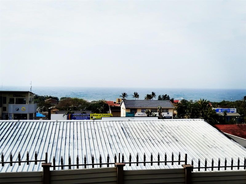 Elevated view overlooking the surrounding neighborhood and coastline, featuring a metal roof in the foreground with security spikes.