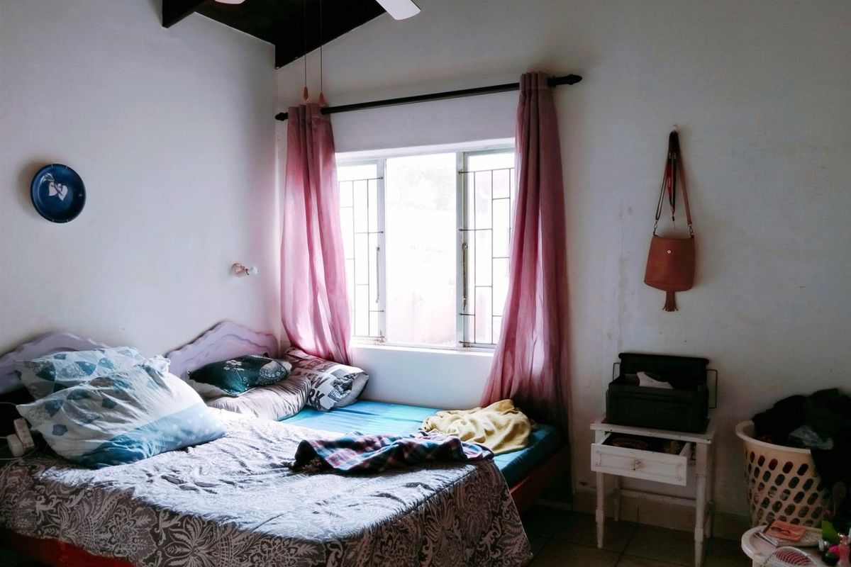 A bedroom featuring exposed timber ceiling beams, tiled flooring, and a window with security bars, requiring some cosmetic attention to the walls.