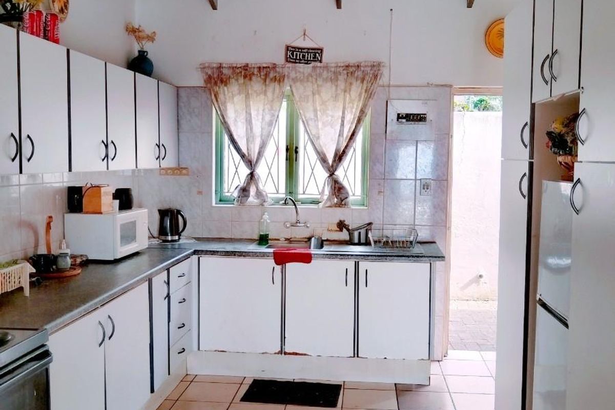 A functional kitchen featuring white cabinetry, tiled flooring, and exposed timber ceiling beams, offering a dated aesthetic with potential for modernization.