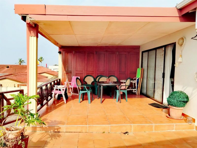 A covered outdoor patio featuring tiled flooring, a wooden balustrade, and direct access to the interior through a sliding glass door.