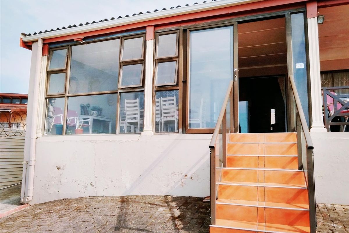 Rear exterior view of the apartment featuring a tiled staircase with metal handrails, aluminium window frames, and a sliding glass door entrance.