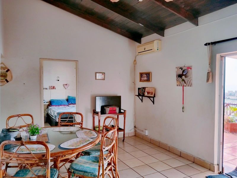 Open-plan living area featuring exposed timber ceiling beams, ceramic floor tiles, and a split-system air conditioner, with direct access to an outdoor balcony.