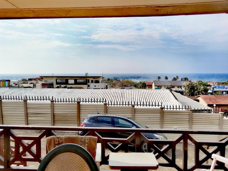 An elevated view overlooking the surrounding neighborhood and distant ocean horizon, captured from a balcony with a wooden railing.