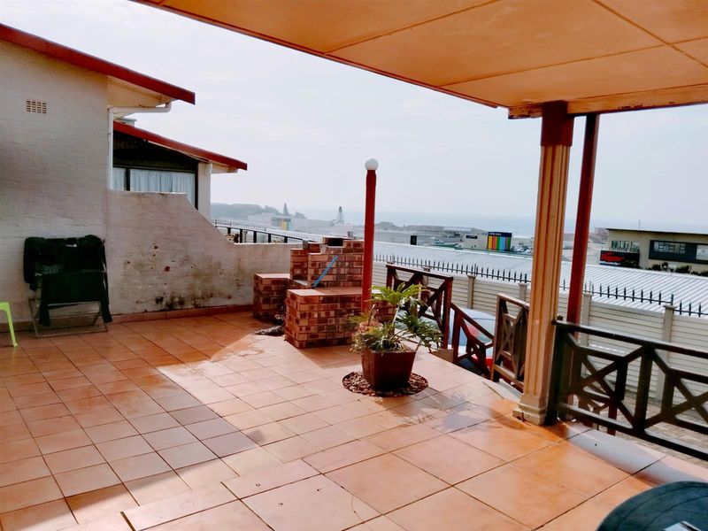 Spacious covered patio featuring tiled flooring, a built-in brick braai, and wooden balustrades, offering an outdoor entertainment area with coastal views.