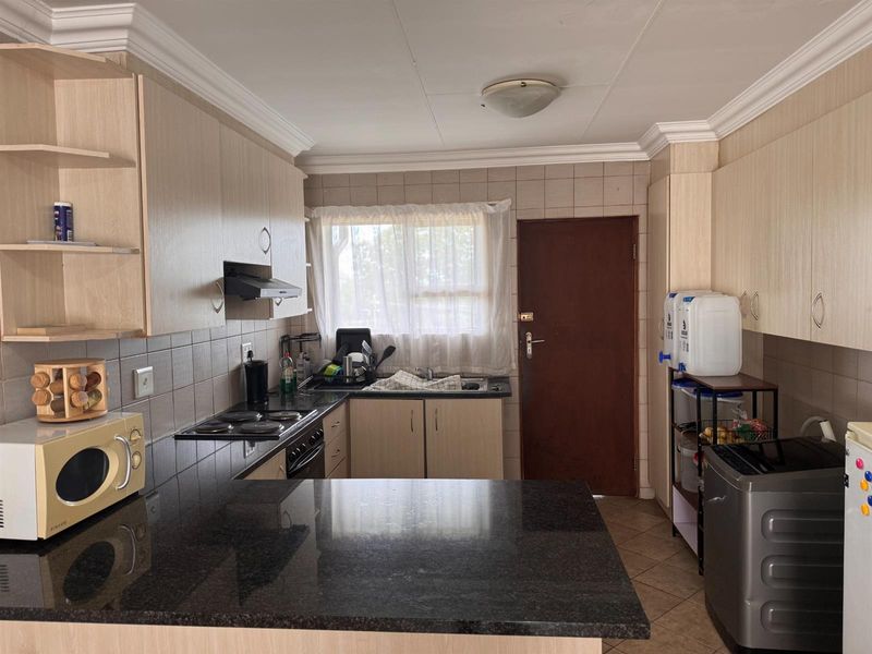 Functional kitchen featuring laminate cabinetry, granite countertops, electric hob, extractor fan, and tiled backsplash with direct access to an exterior door.