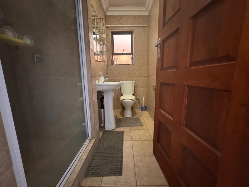 A functional bathroom featuring a pedestal basin, a shower enclosure, and neutral ceramic tiling throughout.