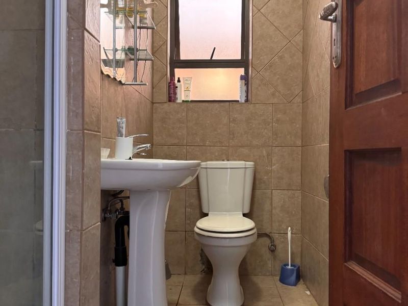 A compact bathroom featuring a pedestal basin, toilet, and shower enclosure with neutral wall and floor tiling.