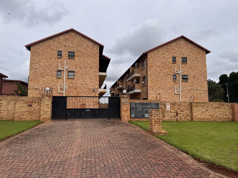 Front view of the L'Connoisseur apartment complex featuring a face brick facade, paved driveway, and secure gated entrance.