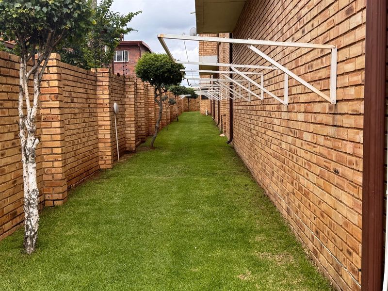 A well-maintained narrow rear garden area featuring a brick boundary wall, lawn, and wall-mounted washing line infrastructure along the building exterior.