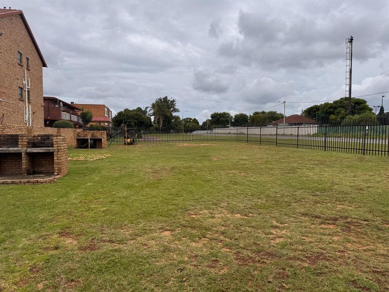 A spacious communal garden area featuring a brick built-in braai and secure metal perimeter fencing.