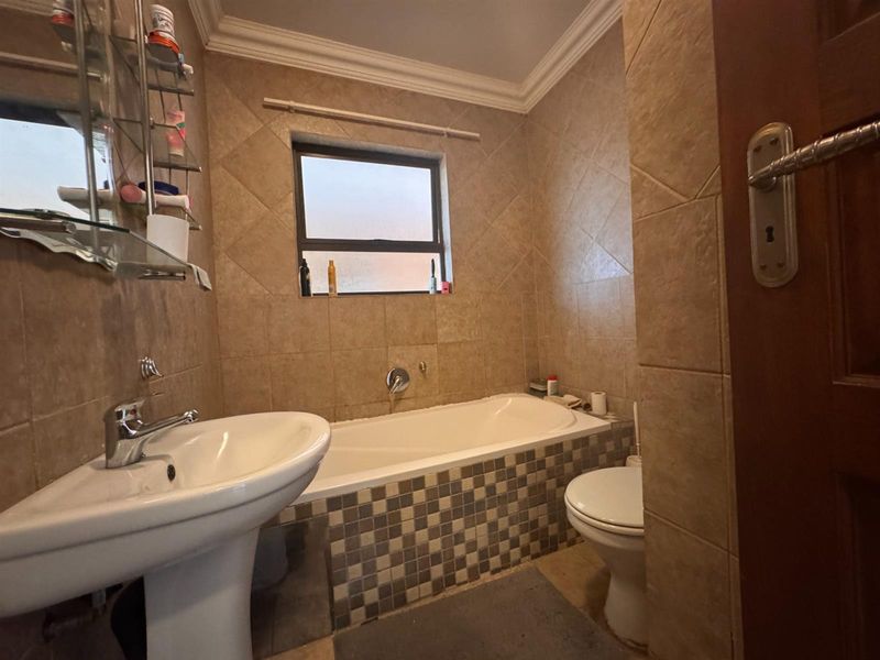 A functional bathroom featuring a pedestal basin, bathtub, and toilet with neutral wall and floor tiling throughout.