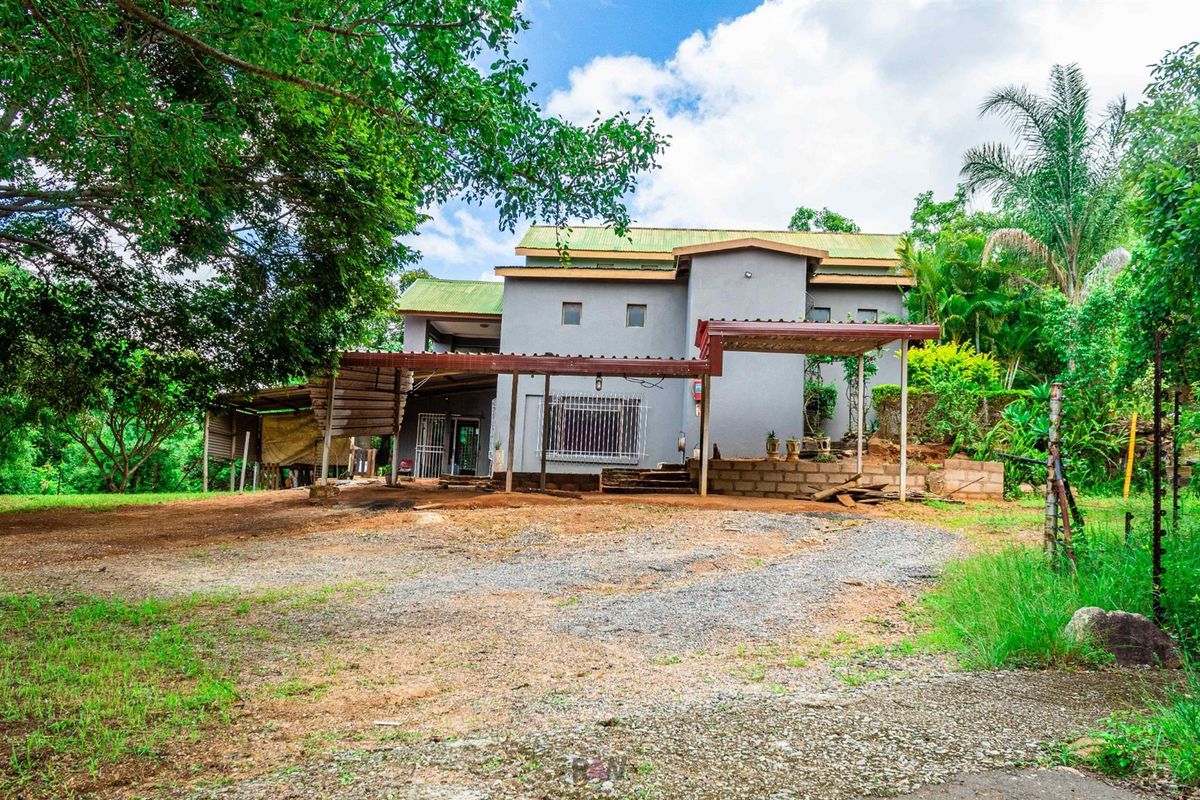 Exterior view of a multi-level residential property featuring a gravel driveway, covered patio area, and established garden surroundings.