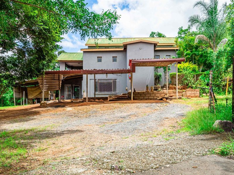 Exterior view of a multi-level residential property featuring a covered patio area, metal roofing, and a large unpaved driveway space.