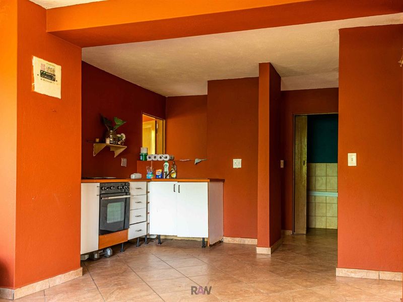 A compact kitchen area featuring built-in cabinetry, an integrated oven, and tiled flooring, finished with bold orange wall paint.