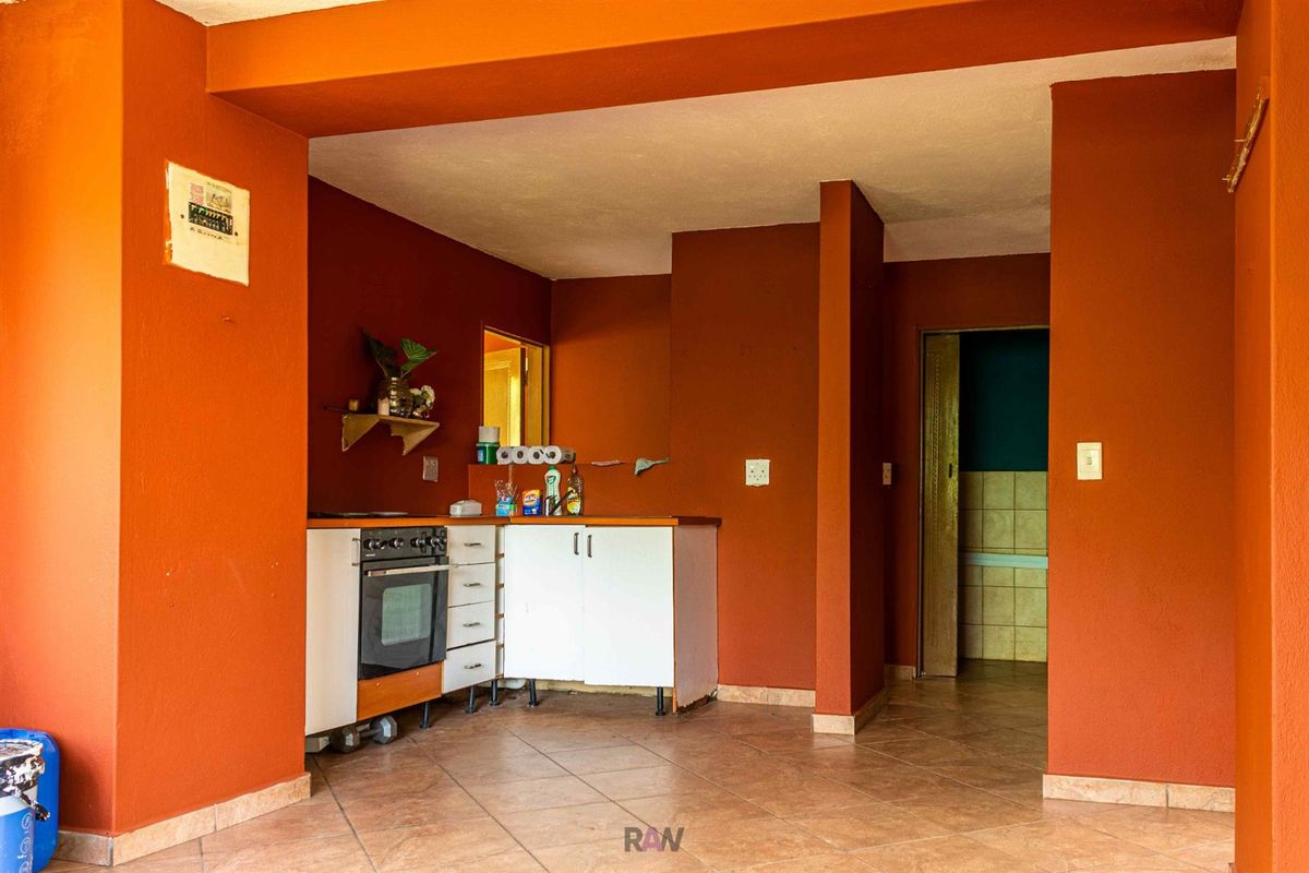 A compact kitchen area featuring built-in cabinetry, an integrated oven, and tiled flooring, finished with bold orange wall paint.