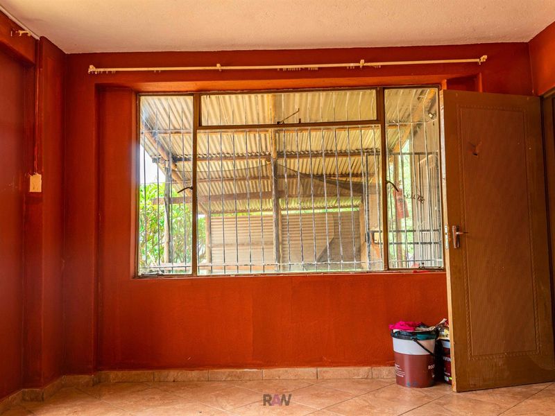 An empty room featuring terracotta-toned walls, tiled flooring, and a large window fitted with security bars, offering a blank canvas for renovation.
