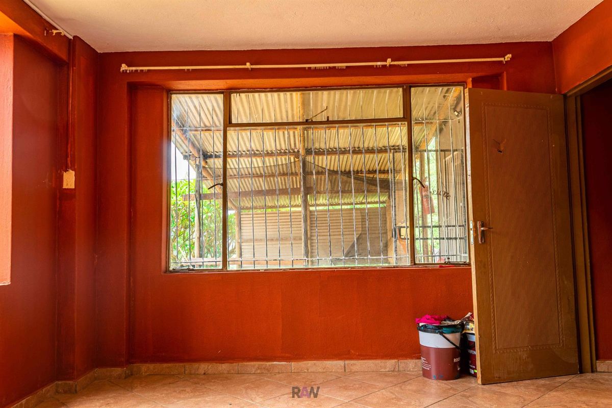 An empty room featuring terracotta-toned walls, tiled flooring, and a large window fitted with security bars, offering a blank canvas for renovation.