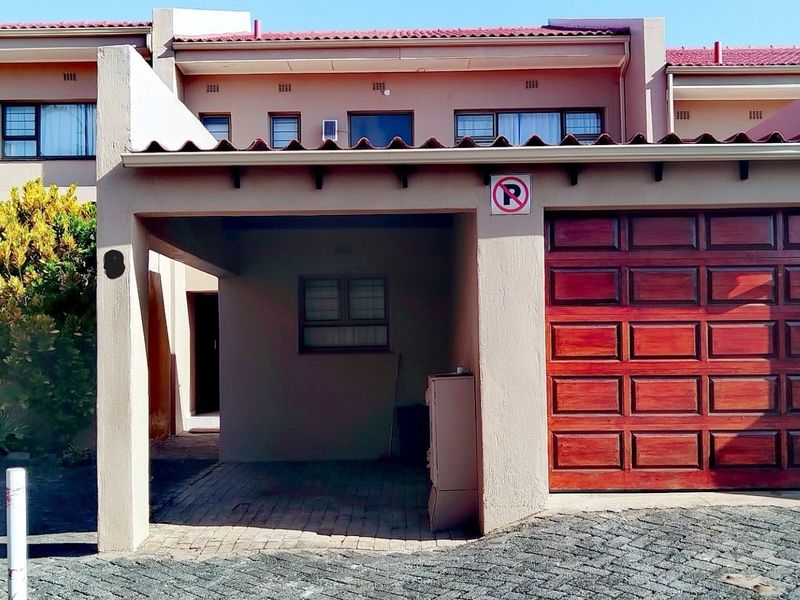 Front elevation of the apartment featuring a covered carport, a wooden garage door, and paved driveway access.