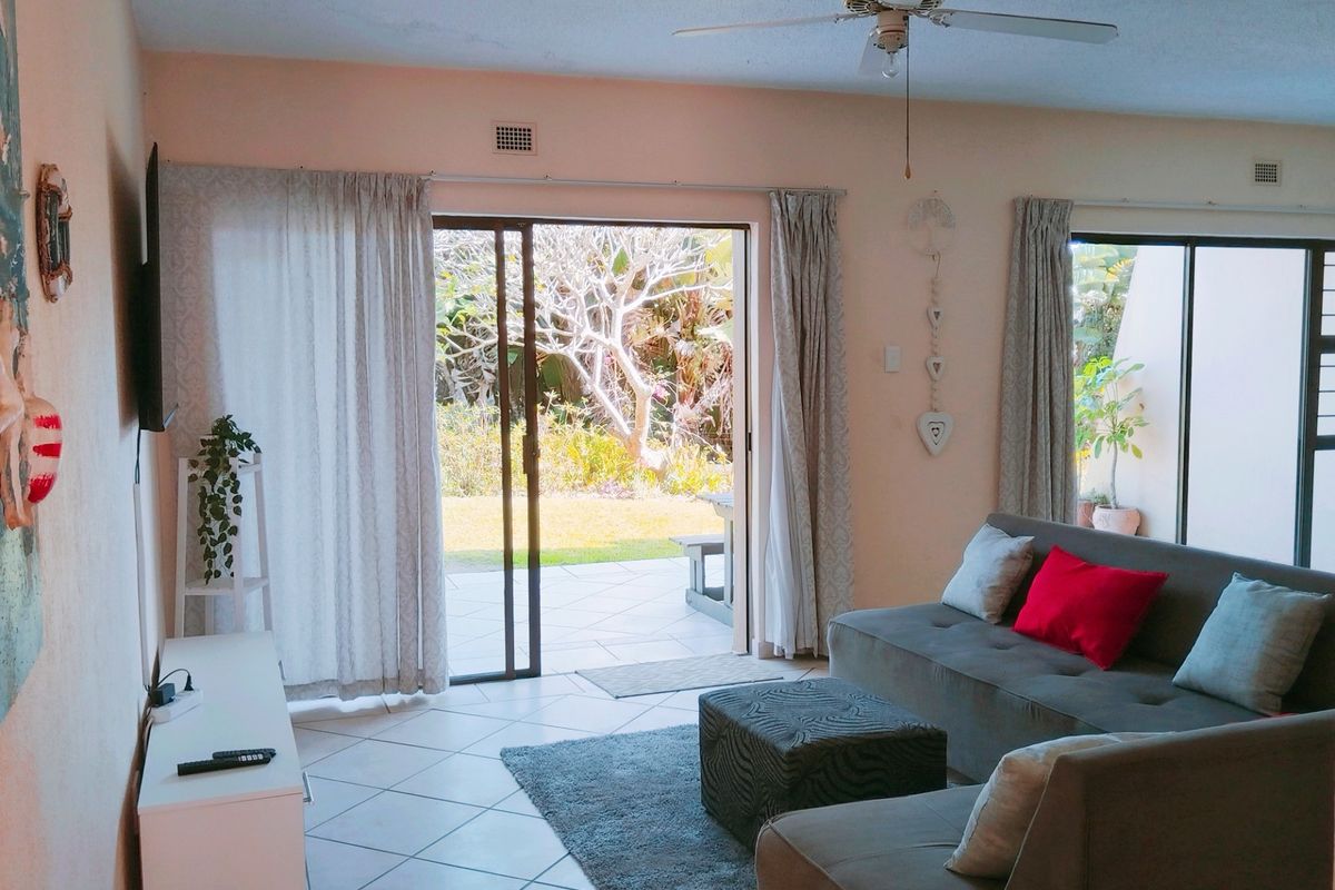 A bright living room featuring tiled flooring, a ceiling fan, and large sliding glass doors that provide direct access to the outdoor patio area.