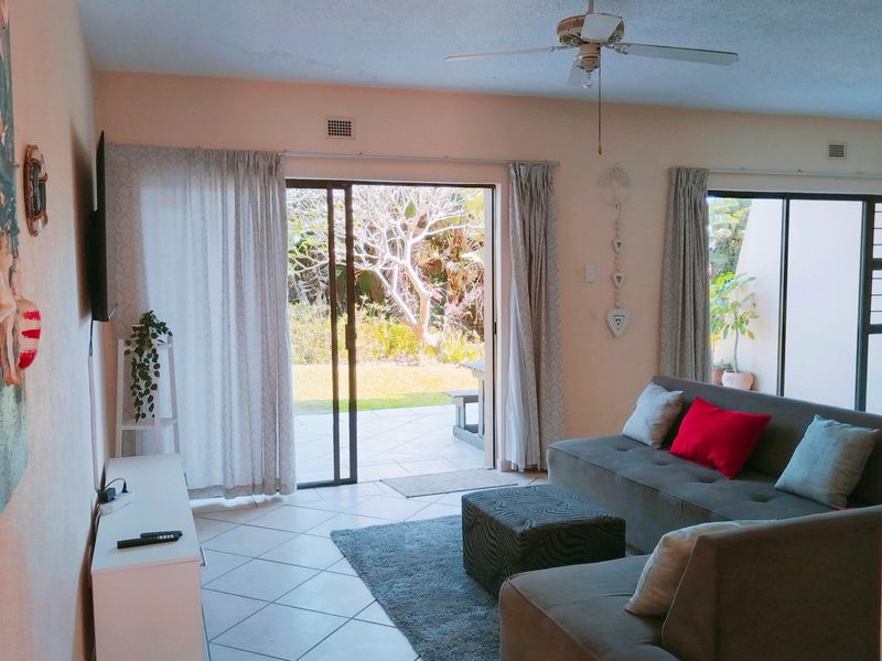 A bright living room featuring tiled flooring, a ceiling fan, and large sliding glass doors that provide direct access to the outdoor patio area.