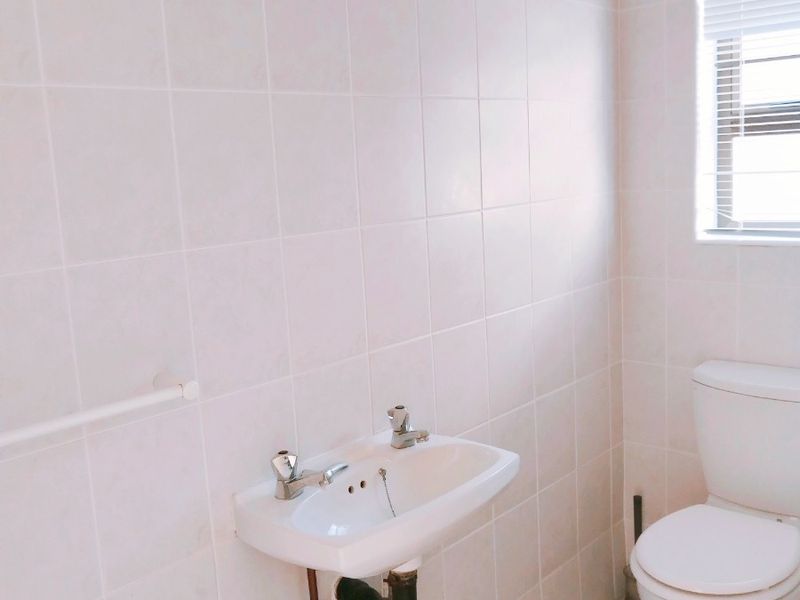 A functional bathroom featuring a wall-mounted basin, standard toilet, and fully tiled walls and flooring with natural light from a window.