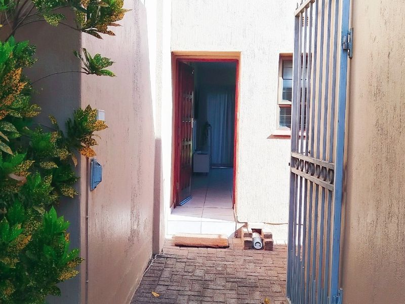 An exterior view of the apartment entrance featuring a paved walkway, security gate, and access to the main living area.