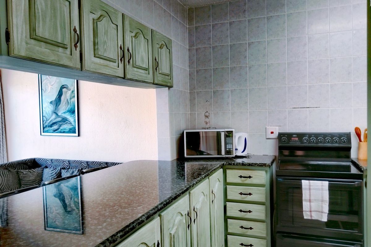 A functional kitchen featuring granite countertops, tiled backsplash, and traditional cabinetry with a convenient pass-through window to the living area.