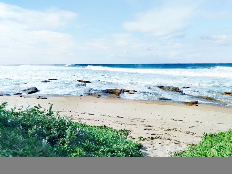 A scenic view of the ocean coastline featuring sandy beach, rocky outcrops, and coastal vegetation.