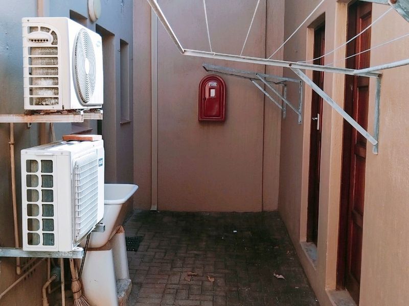 A functional outdoor utility area featuring a paved floor, wall-mounted drying rack, utility sink, and air conditioning units.