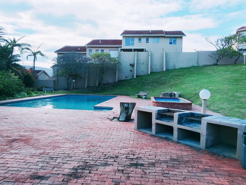 Outdoor pool area featuring a swimming pool, built-in braai, and brick paved patio set against a landscaped garden and perimeter wall.