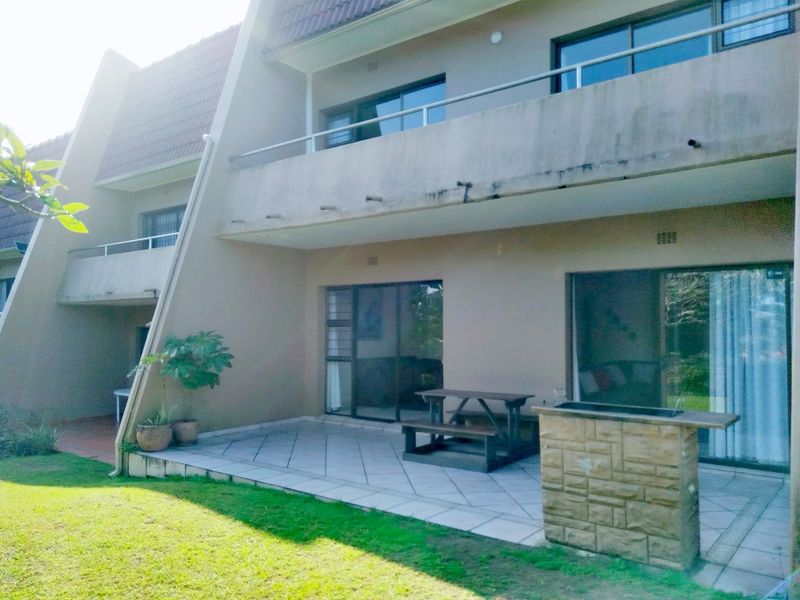 Rear view of the apartment featuring a tiled patio with a built-in stone braai, sliding door access, and an upper-level balcony.