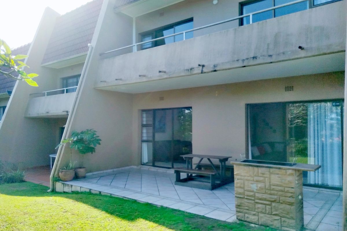 Rear view of the apartment featuring a tiled patio with a built-in stone braai, sliding door access, and an upper-level balcony.