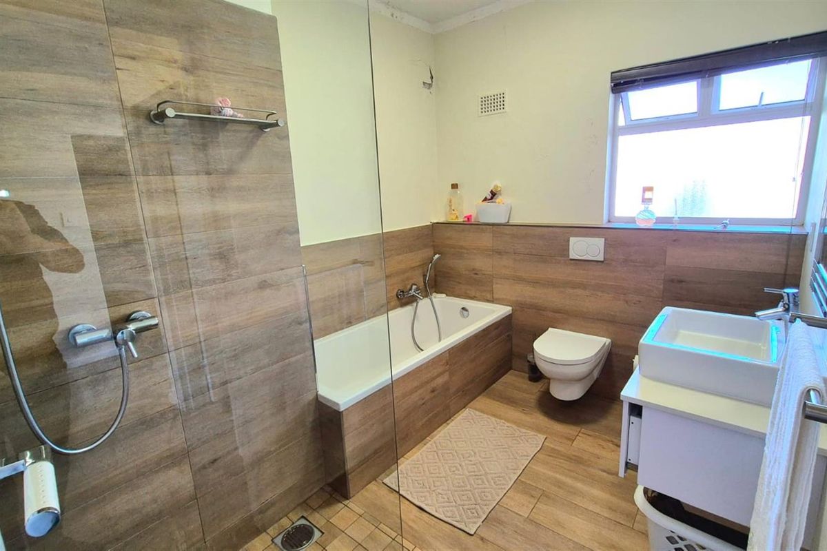 Modern bathroom featuring wood-look tile finishes, a glass-enclosed walk-in shower, a built-in bathtub, a wall-mounted toilet, and a contemporary vanity basin.