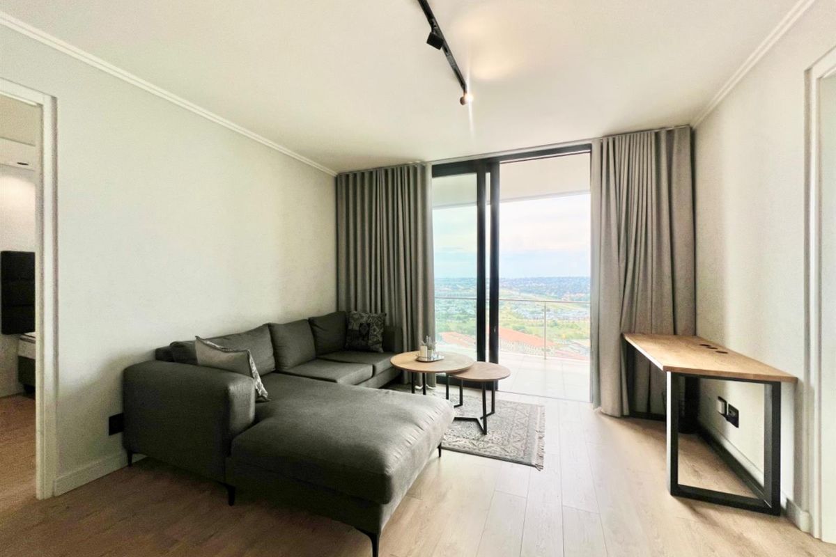 Modern living room featuring light wood-look flooring, track lighting, and large sliding glass doors opening to a balcony with expansive views.