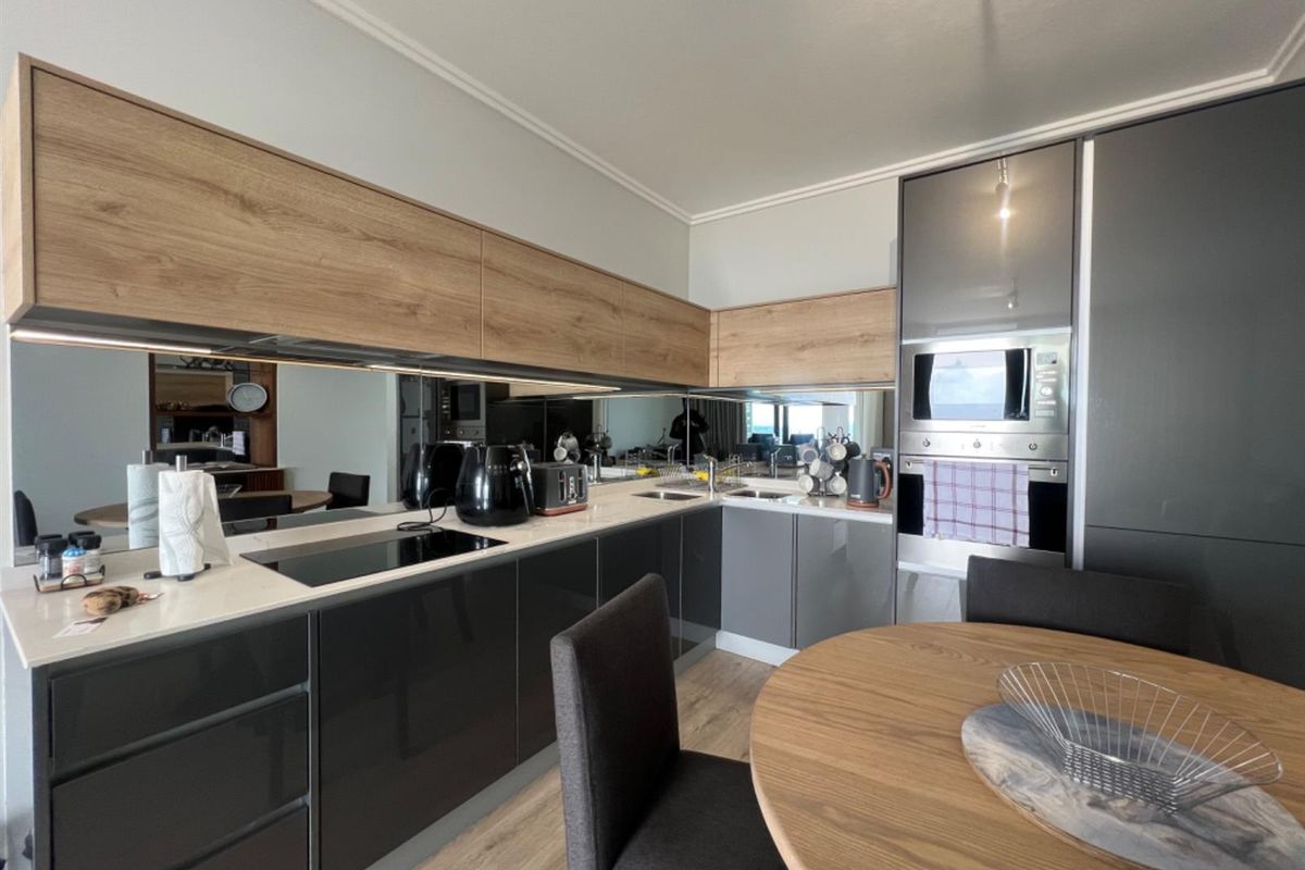 Modern kitchen featuring sleek grey cabinetry, wood-tone upper cabinets, integrated oven and microwave, and a mirrored backsplash.
