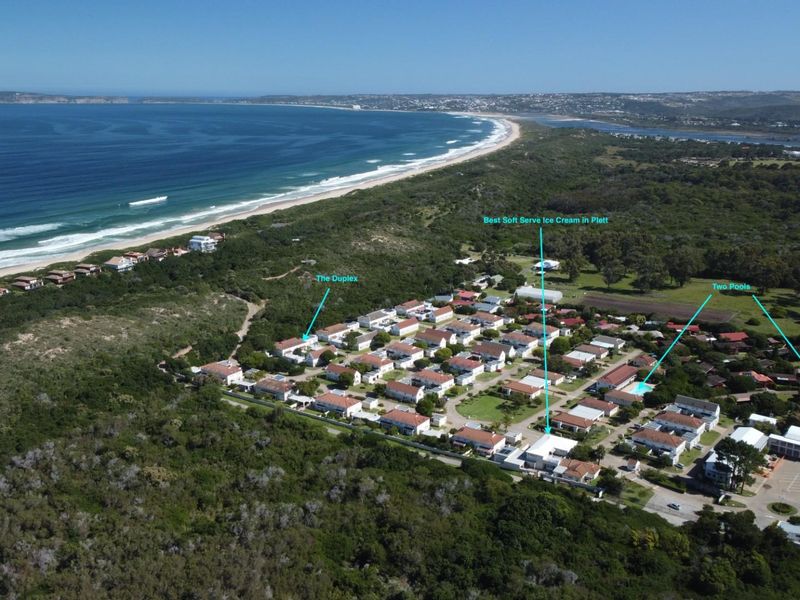 Aerial view of the residential complex situated near the coastline, featuring communal swimming pools and proximity to the beach.