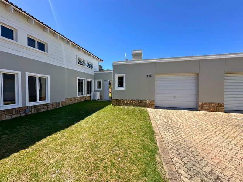 Front exterior view of the property featuring a paved driveway, garage access, stone cladding accents, and a well-maintained lawn area.