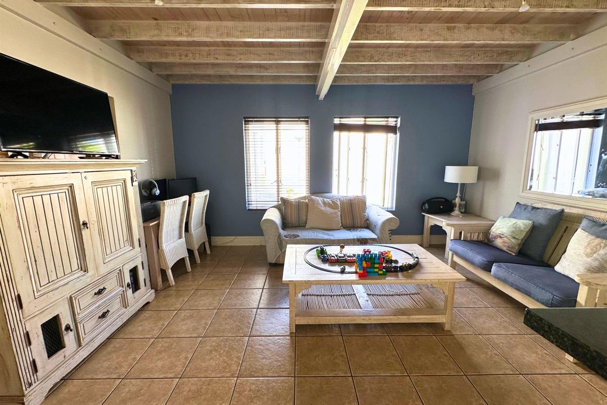 A comfortable living room featuring exposed timber ceiling beams, tiled flooring, and natural light through venetian blinds.