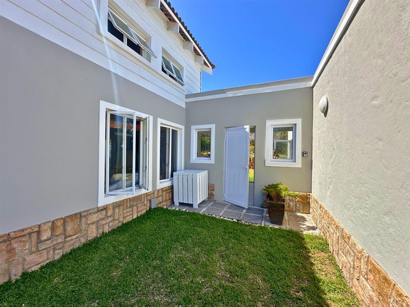 A well-maintained rear courtyard featuring stone cladding, a small lawn, and paved access to the building entrance.